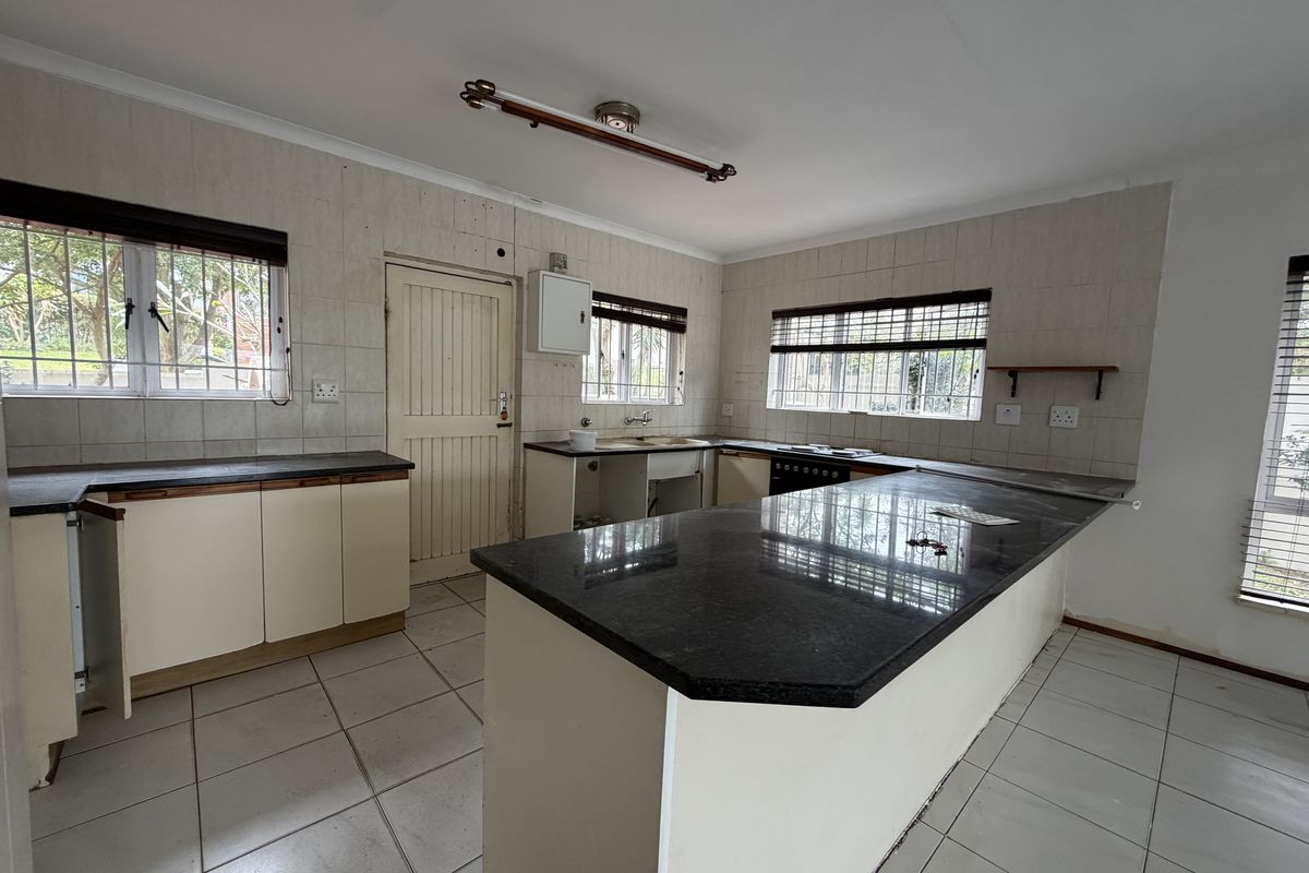A spacious, empty kitchen featuring granite countertops, tiled flooring, and ample cabinetry, offering a blank canvas for renovation and modernization.