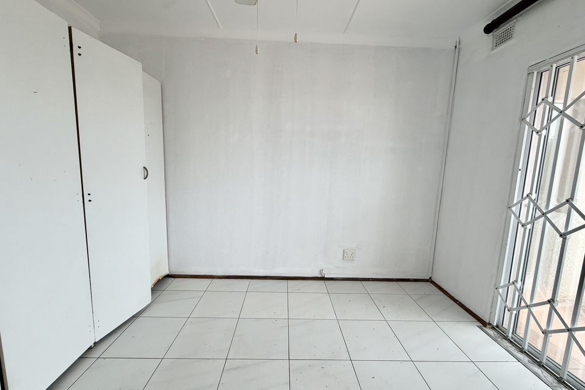An empty bedroom featuring white tiled flooring, a built-in wardrobe, and a sliding door with a security gate.