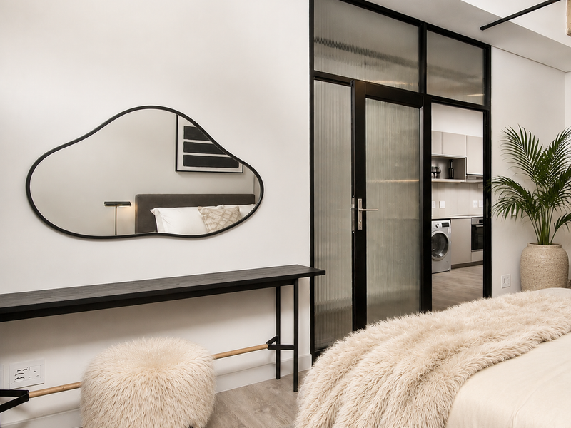 Modern bedroom featuring laminate flooring, an exposed concrete ceiling beam, and a stylish black metal-framed glass door leading to an adjacent kitchen area.
