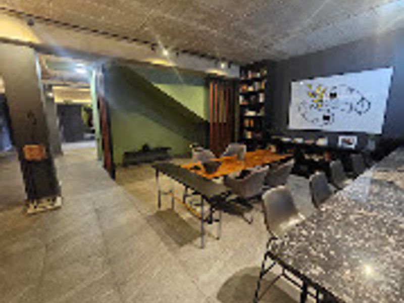Modern open-plan living area featuring an exposed concrete ceiling, recessed track lighting, built-in shelving, and a stone-topped breakfast bar.