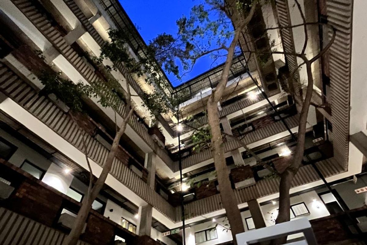 A striking view looking up through the central atrium of an apartment complex, featuring multi-level balconies, exposed brick architecture, and mature trees.
