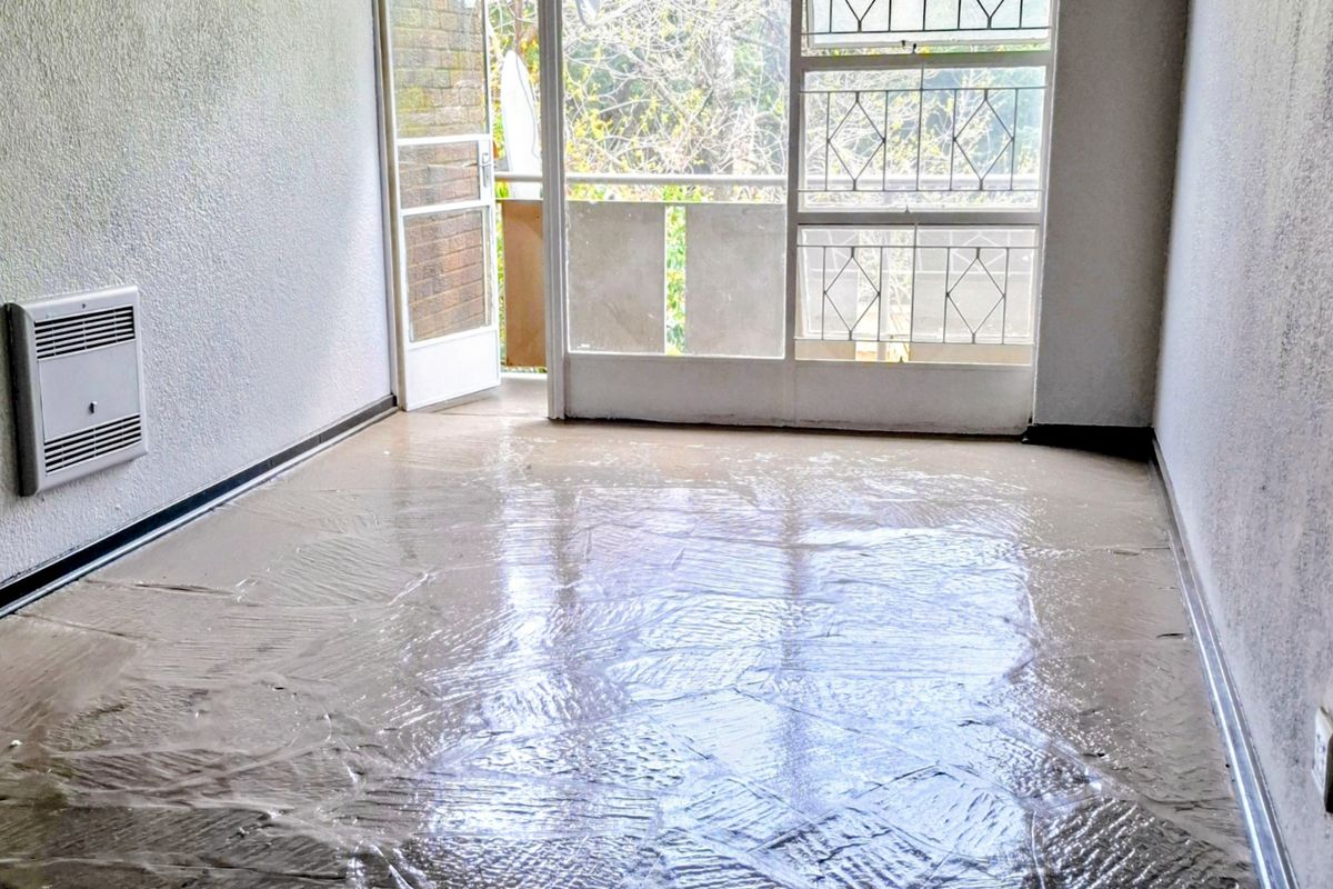 An empty living room featuring a wall-mounted heater, security gate, and access to a balcony, currently requiring flooring and wall finish updates.