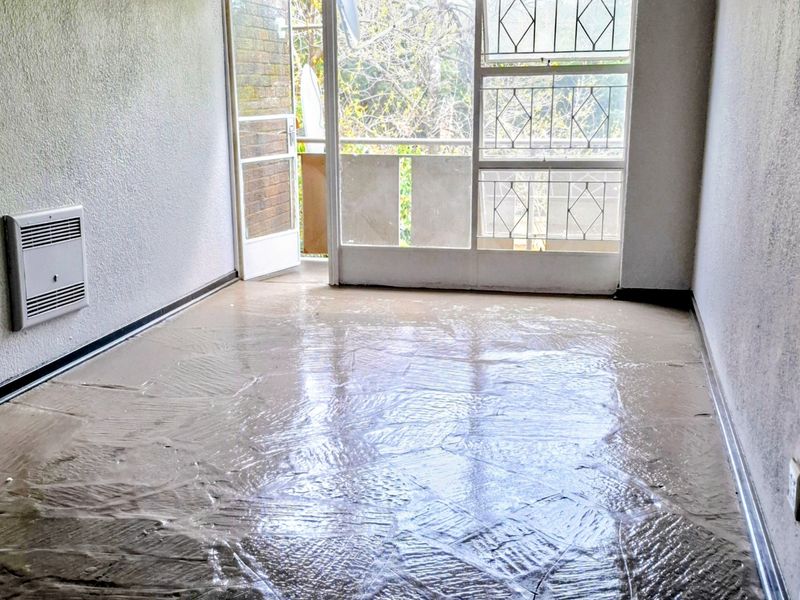 An empty living room featuring a wall-mounted heater, security gate, and access to a balcony, currently requiring flooring and wall finish updates.