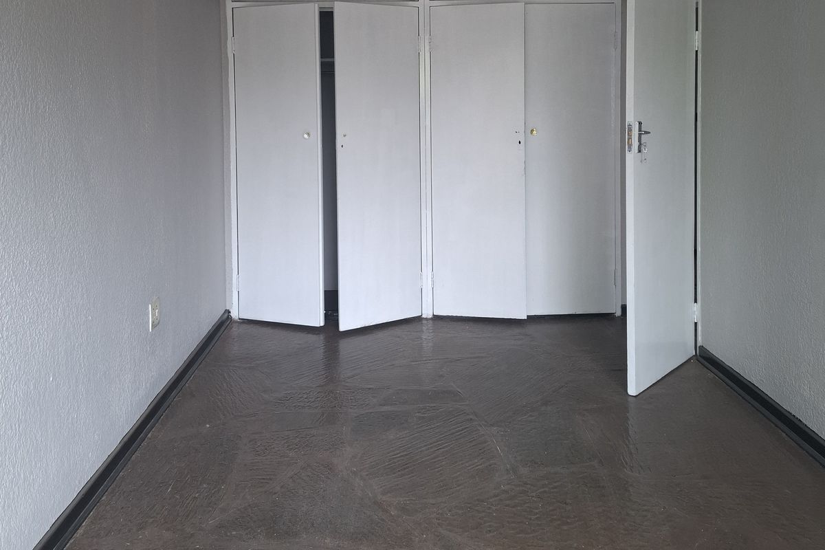 An empty bedroom featuring built-in cupboards with overhead storage and stone tile flooring.