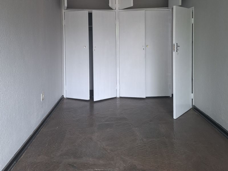 An empty bedroom featuring built-in cupboards with overhead storage and stone tile flooring.