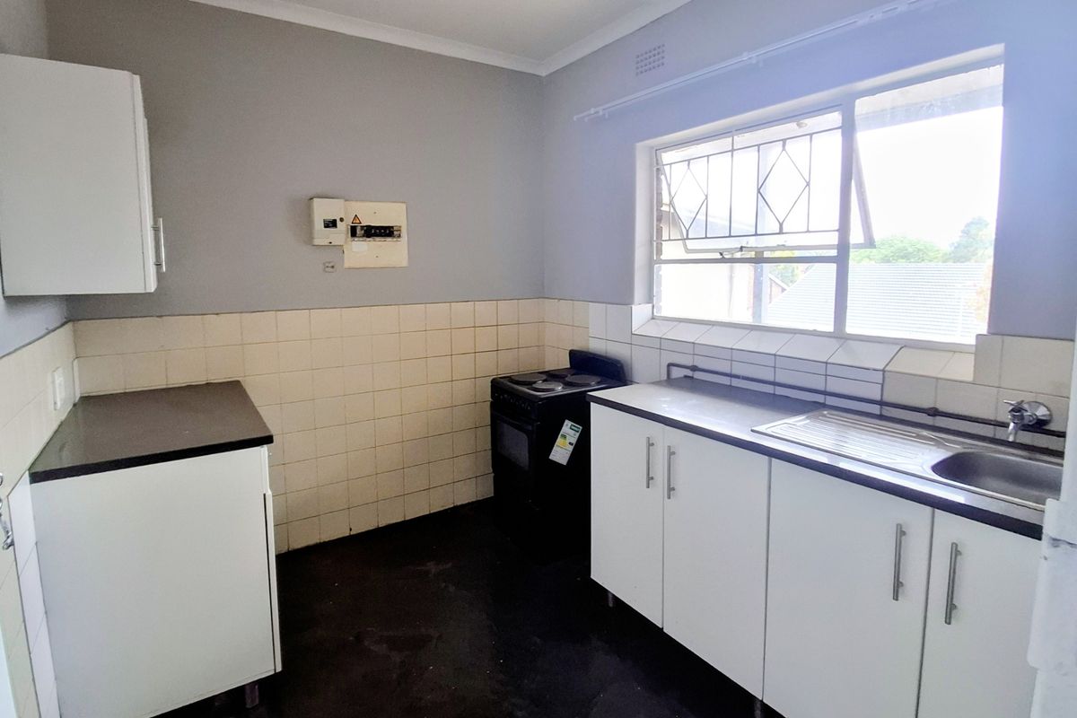 A functional kitchen featuring white cabinetry, a stainless steel sink, tiled splashbacks, and a freestanding stove, offering a blank canvas for potential updates.