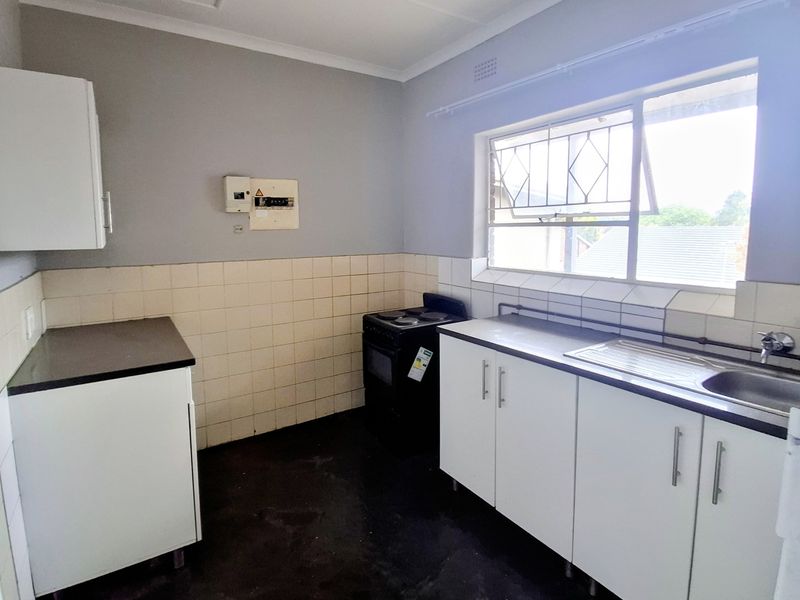 A functional kitchen featuring white cabinetry, a stainless steel sink, tiled splashbacks, and a freestanding stove, offering a blank canvas for potential updates.
