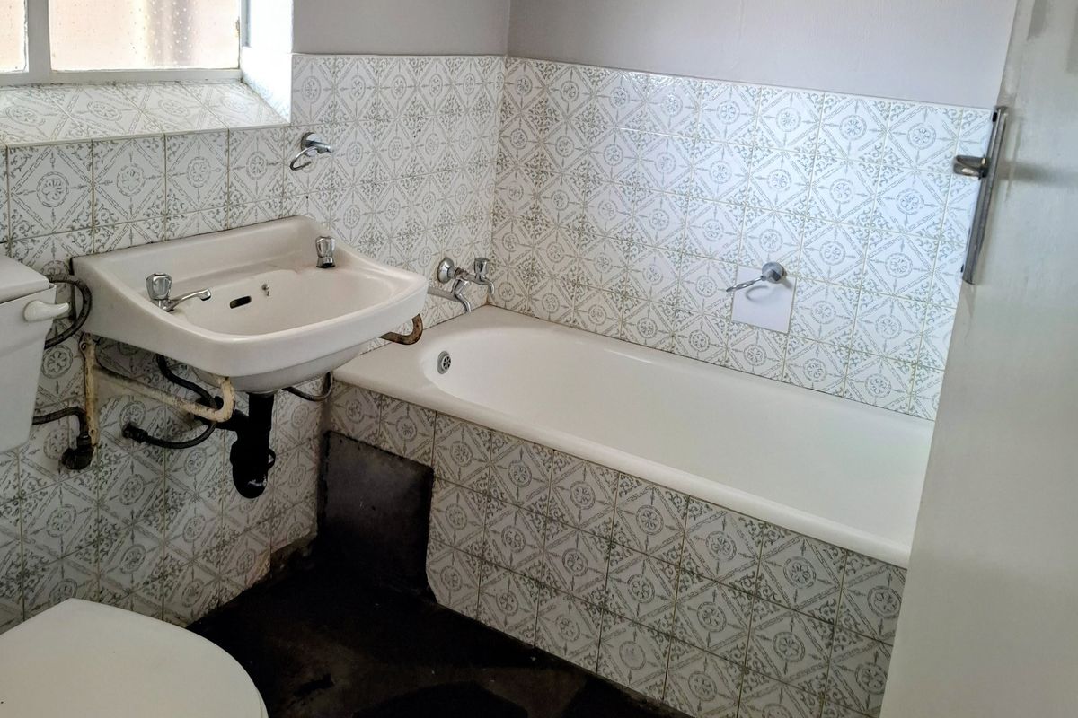A dated bathroom featuring a standard bathtub, wall-mounted basin, and toilet, requiring significant renovation and modernization of fixtures and finishes.