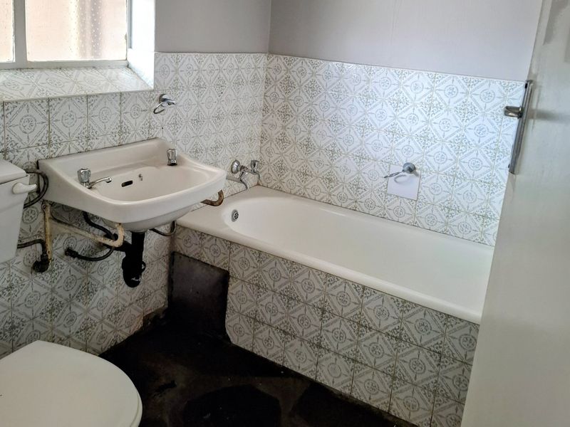 A dated bathroom featuring a standard bathtub, wall-mounted basin, and toilet, requiring significant renovation and modernization of fixtures and finishes.