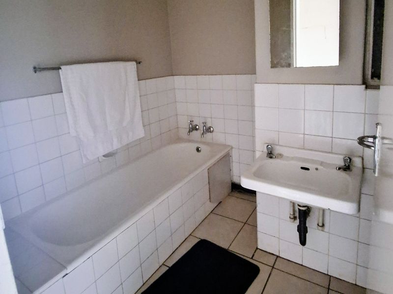 A functional bathroom featuring a standard bathtub, wall-mounted basin, and tiled finishes, offering a blank canvas for potential modernization and renovation.