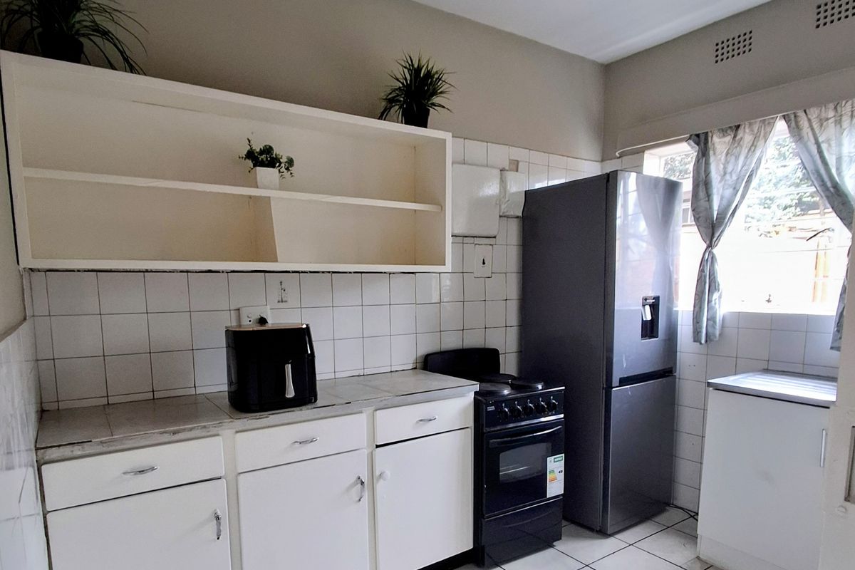 A functional kitchen featuring white cabinetry, tiled splashbacks, tiled flooring, and a freestanding stove, offering a practical layout with potential for modern updates.