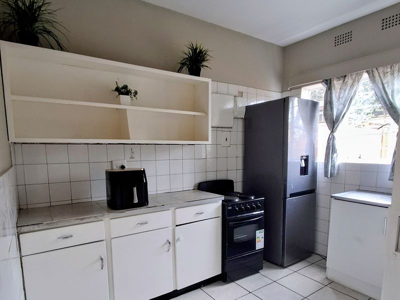 A functional kitchen featuring white cabinetry, tiled splashbacks, tiled flooring, and a freestanding stove, offering a practical layout with potential for modern updates.