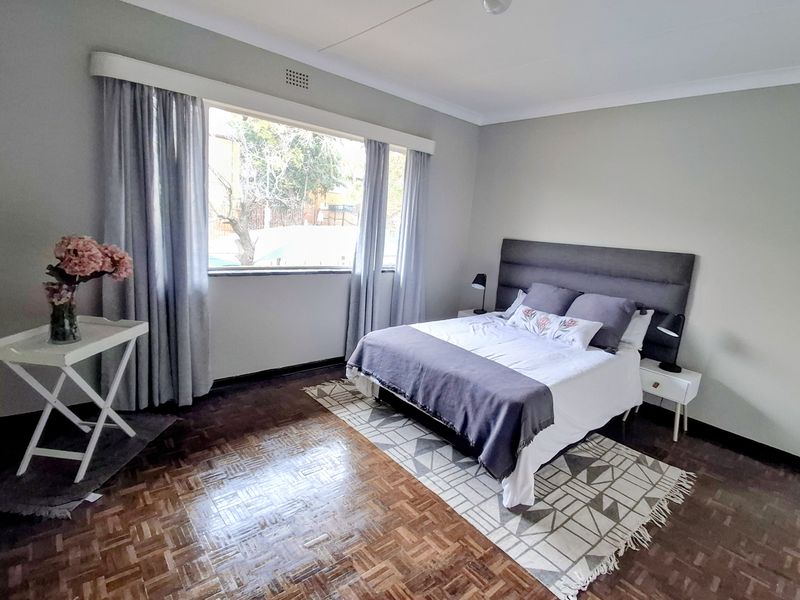 A well-lit bedroom featuring classic parquet flooring, neutral wall tones, and a large window providing natural light.