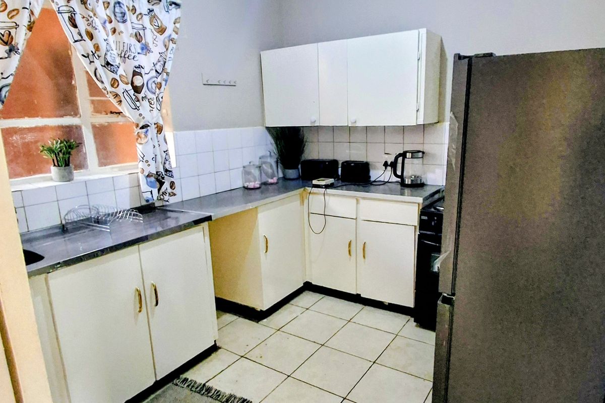 A compact kitchen featuring white built-in cabinetry, tiled backsplash, and laminate countertops, offering a functional layout with potential for modern updates.