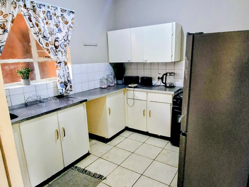 A compact kitchen featuring white built-in cabinetry, tiled backsplash, and laminate countertops, offering a functional layout with potential for modern updates.