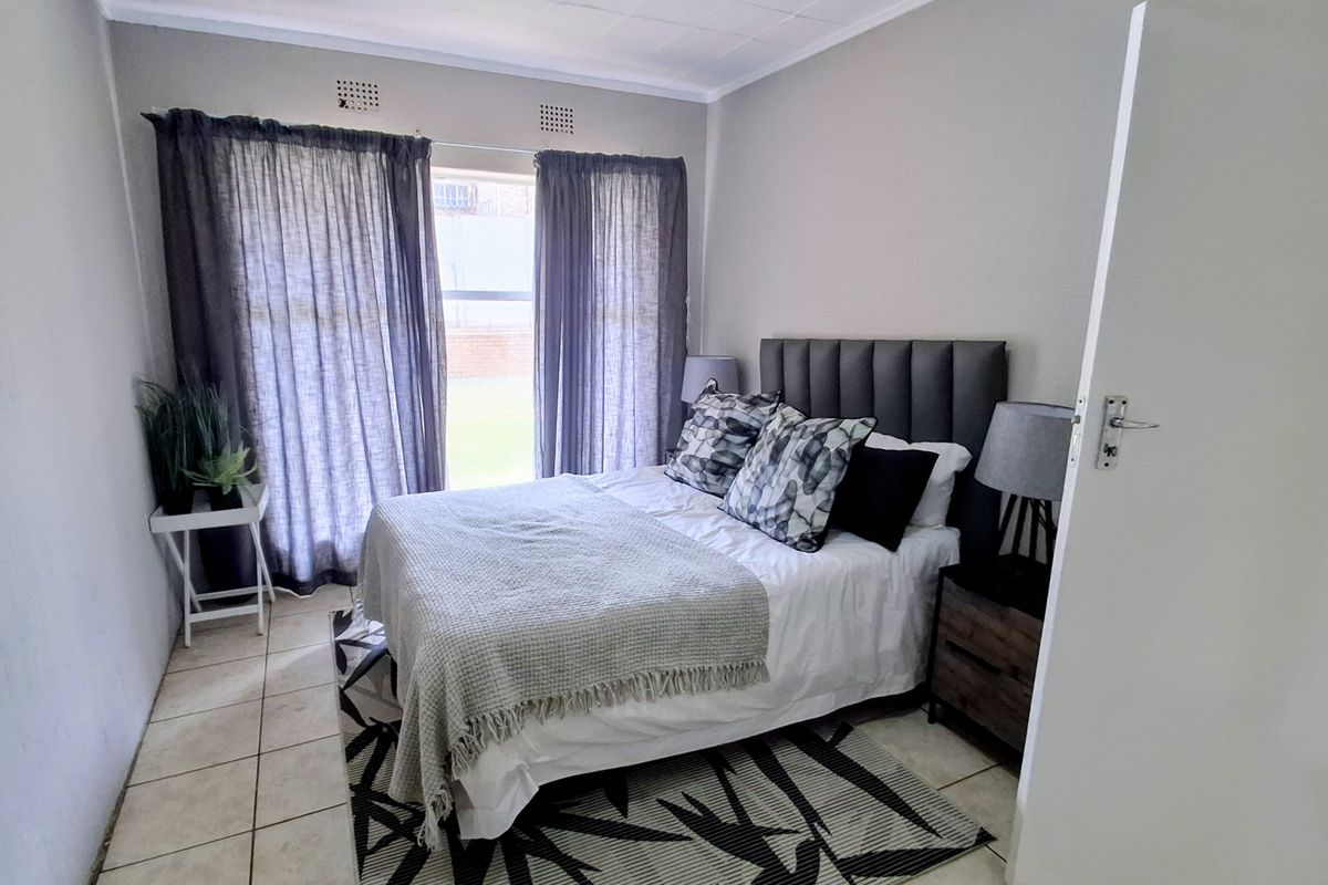 A functional bedroom featuring tiled flooring, neutral wall finishes, and a window with curtain fixtures.
