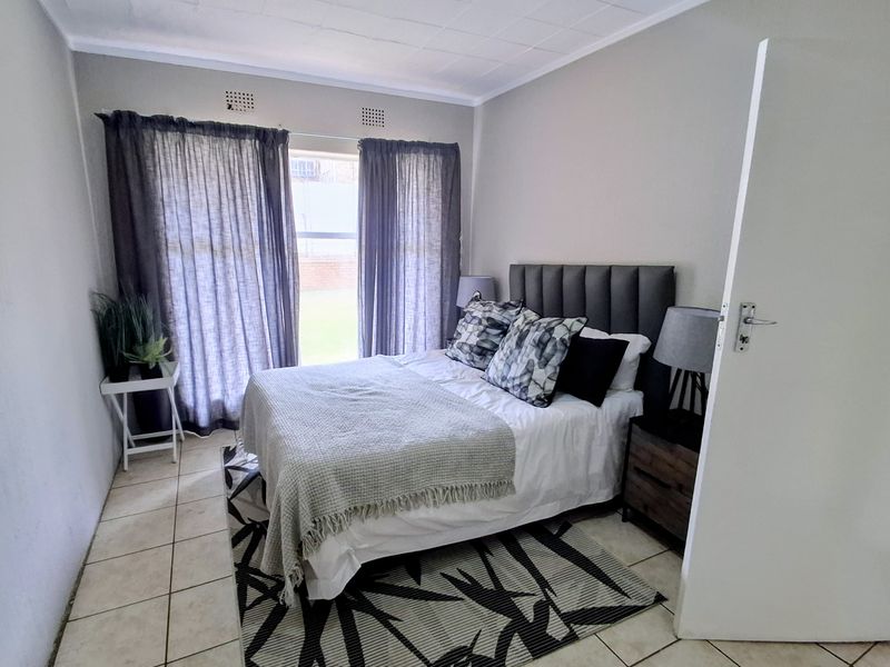 A functional bedroom featuring tiled flooring, neutral wall finishes, and a window with curtain fixtures.