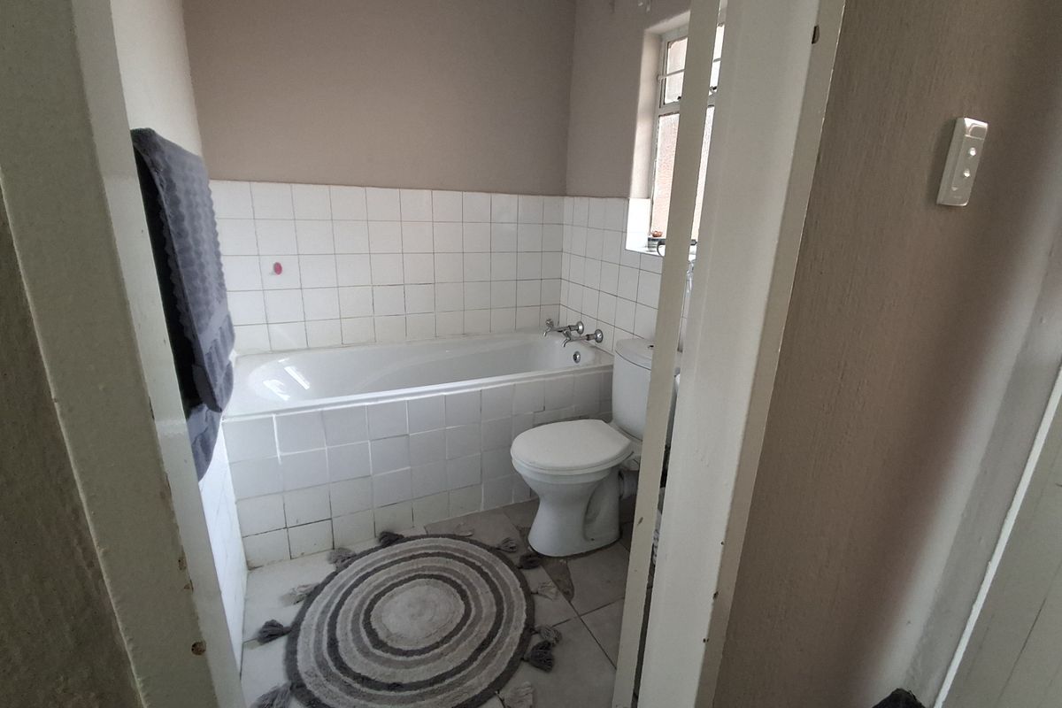 A compact bathroom featuring a standard bathtub, toilet, and tiled splashback, requiring cosmetic updates to modernize the space.