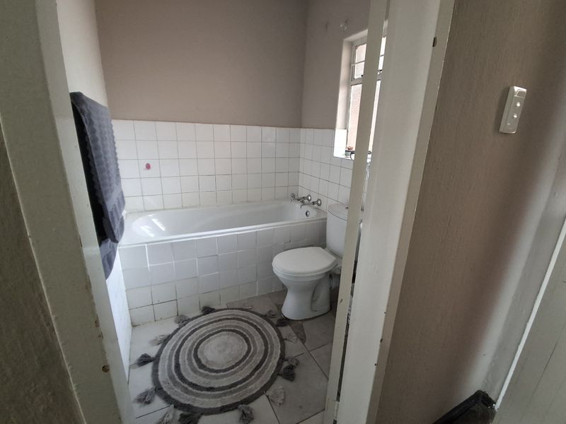 A compact bathroom featuring a standard bathtub, toilet, and tiled splashback, requiring cosmetic updates to modernize the space.