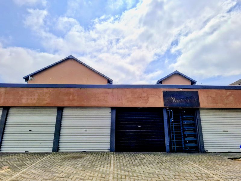 Front elevation of the apartment complex featuring multiple roller shutter garage doors, a secure pedestrian entrance gate, and a paved driveway area.