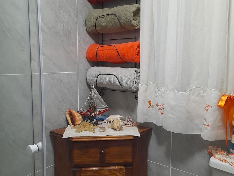 A bathroom corner featuring grey wall tiles, a glass shower screen, and a toilet, accented with a wooden corner cabinet.
