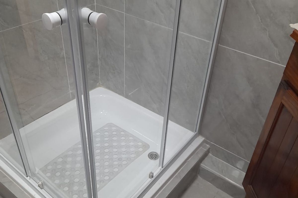 A clean bathroom featuring a modern glass shower enclosure with grey tiled walls and flooring, complemented by a wooden vanity cabinet.