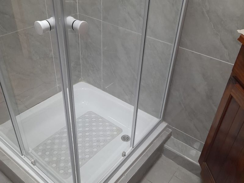 A clean bathroom featuring a modern glass shower enclosure with grey tiled walls and flooring, complemented by a wooden vanity cabinet.