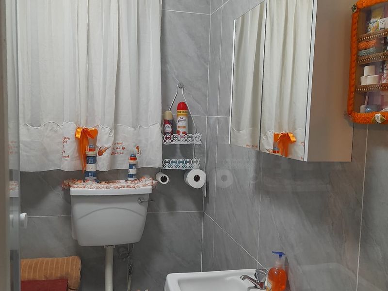 A compact bathroom featuring grey wall tiles, a white washbasin with a mixer tap, and a mirrored medicine cabinet.