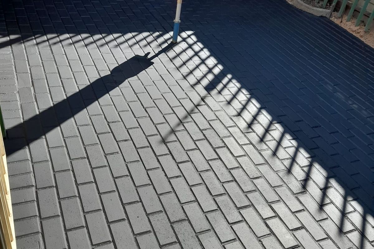 A paved outdoor patio area featuring dark-toned brickwork, enclosed by a brick boundary wall and metal fencing.