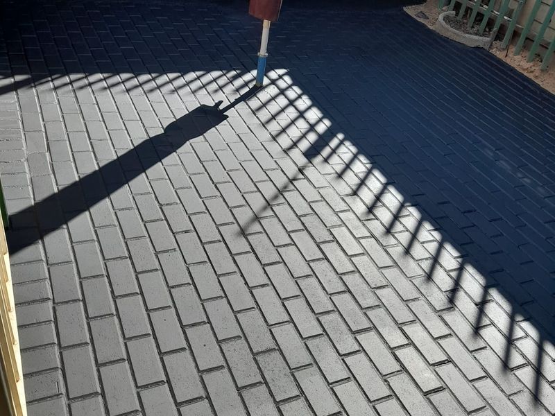 A paved outdoor patio area featuring dark-toned brickwork, enclosed by a brick boundary wall and metal fencing.