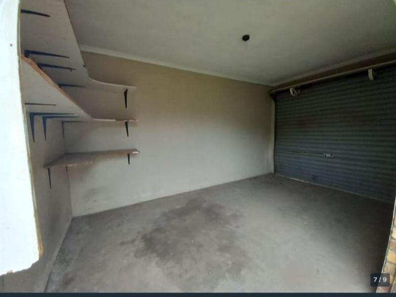 A functional garage space featuring a roller shutter door and built-in wall shelving, providing secure parking and additional storage capacity.