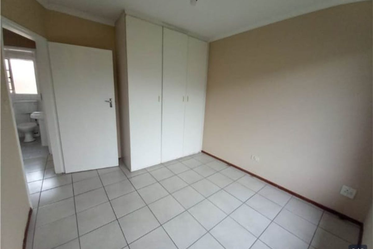 An empty bedroom featuring tiled flooring and built-in cupboards, with an adjacent view into a bathroom area.