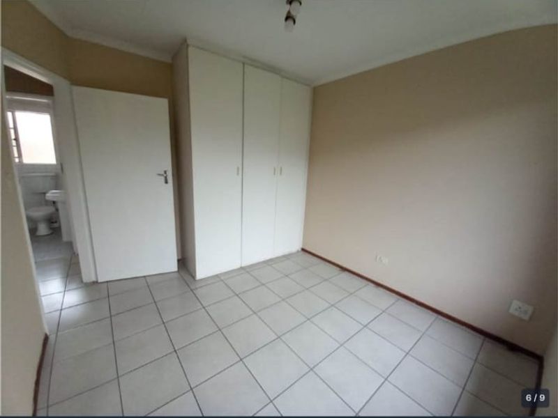 An empty bedroom featuring tiled flooring and built-in cupboards, with an adjacent view into a bathroom area.