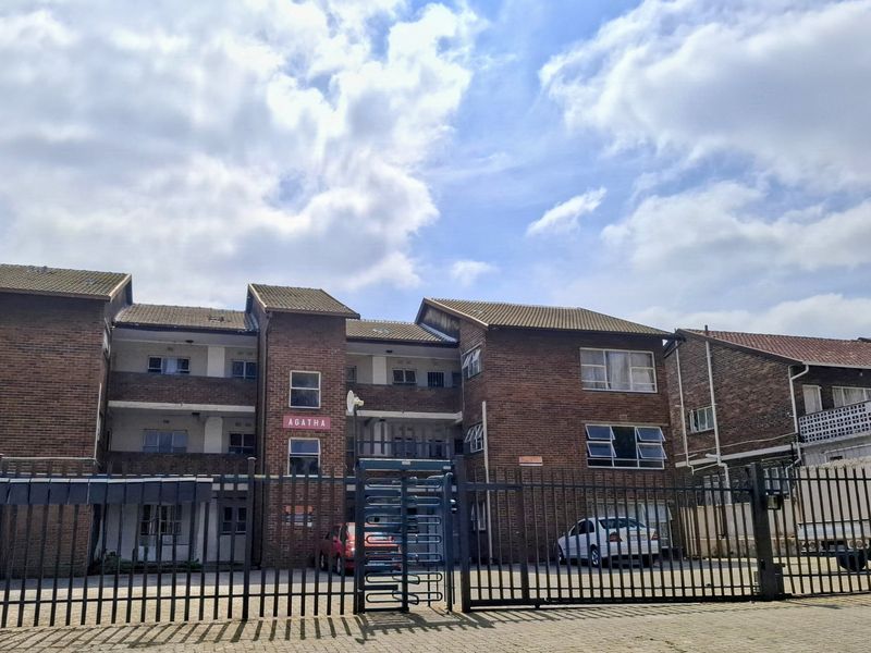 Front elevation of the Agatha apartment complex featuring a face brick facade, secure gated entrance, and paved driveway area.