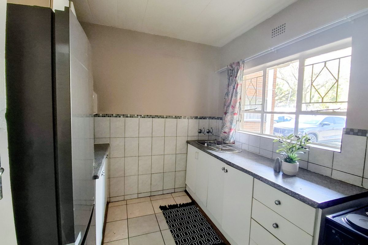 A functional kitchen featuring white cabinetry, laminate countertops, tiled backsplash, and ceramic flooring, with a window providing natural light and street views.