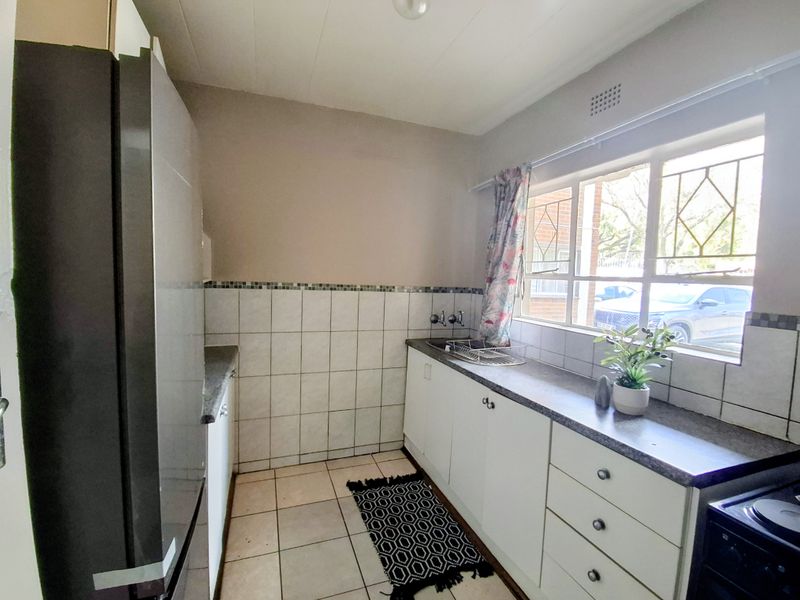 A functional kitchen featuring white cabinetry, laminate countertops, tiled backsplash, and ceramic flooring, with a window providing natural light and street views.