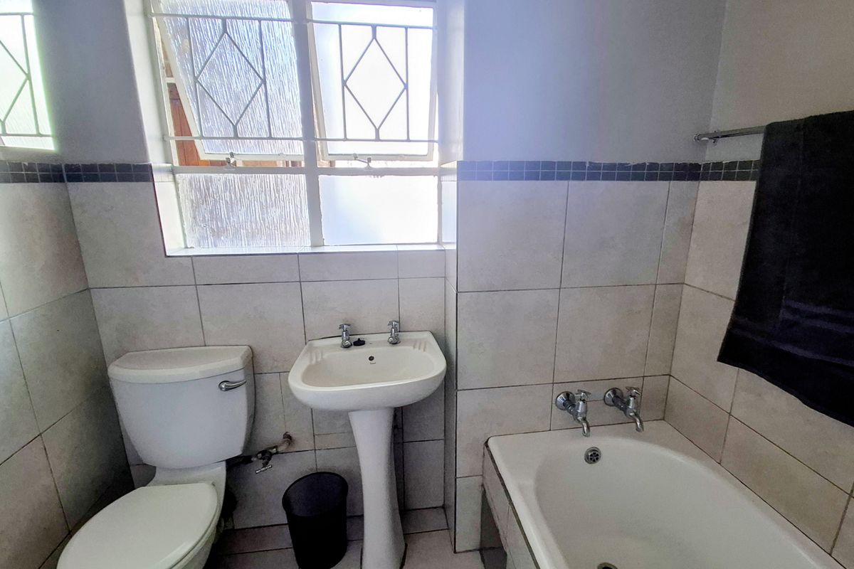 A functional bathroom featuring a pedestal washbasin, toilet, and bathtub with tiled walls and floor, offering a clean and practical layout.