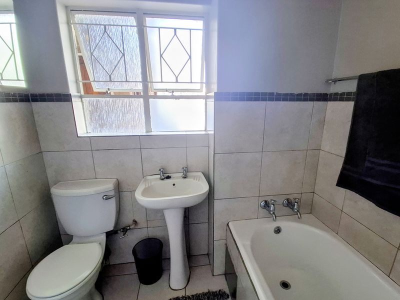 A functional bathroom featuring a pedestal washbasin, toilet, and bathtub with tiled walls and floor, offering a clean and practical layout.