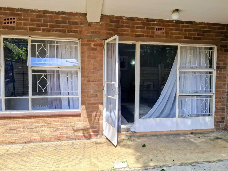 A covered patio area featuring a brick facade, security-barred windows, and a tiled floor, providing direct access to the interior living space.