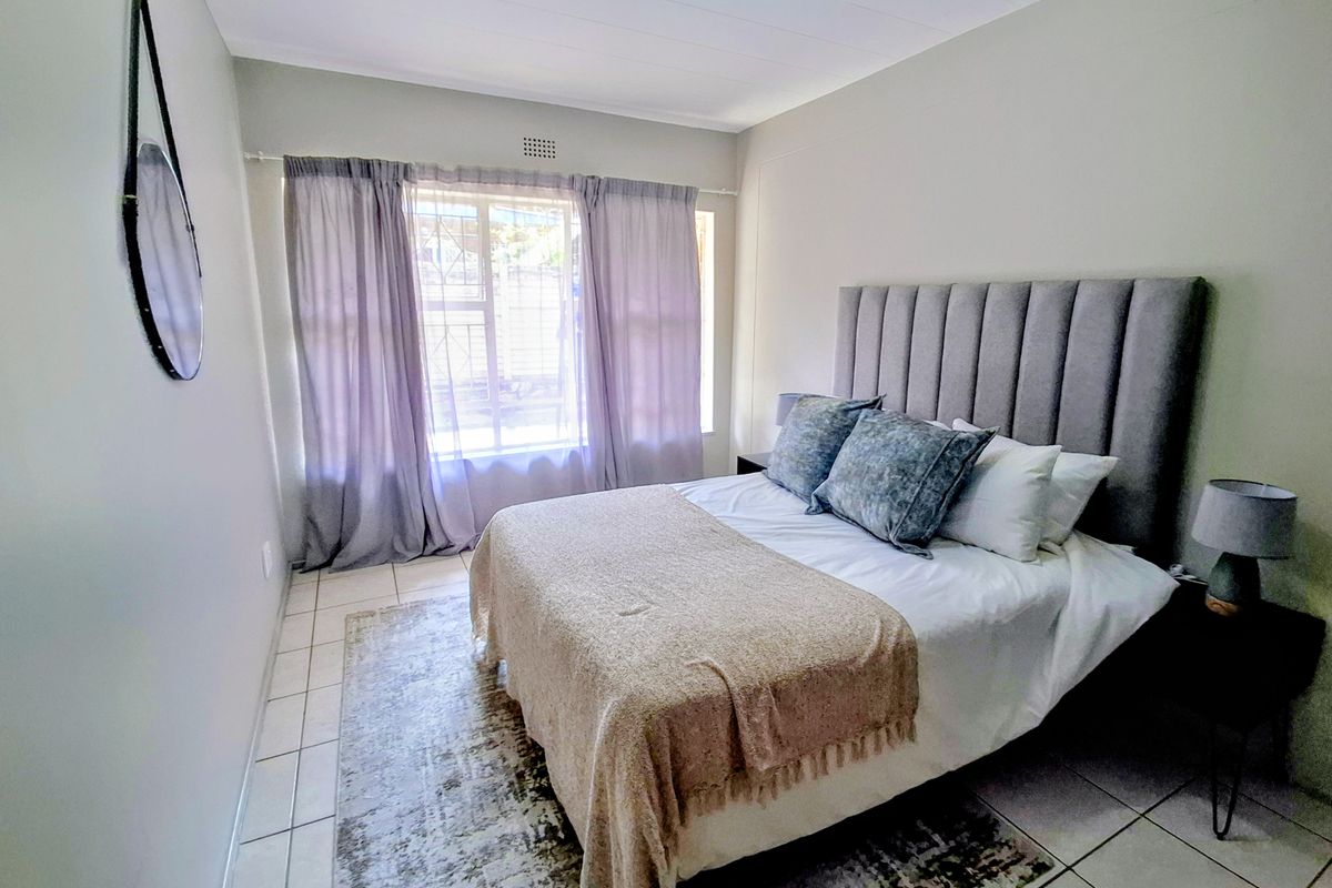 A well-maintained bedroom featuring neutral wall tones, tiled flooring, and a window fitted with security bars for added peace of mind.