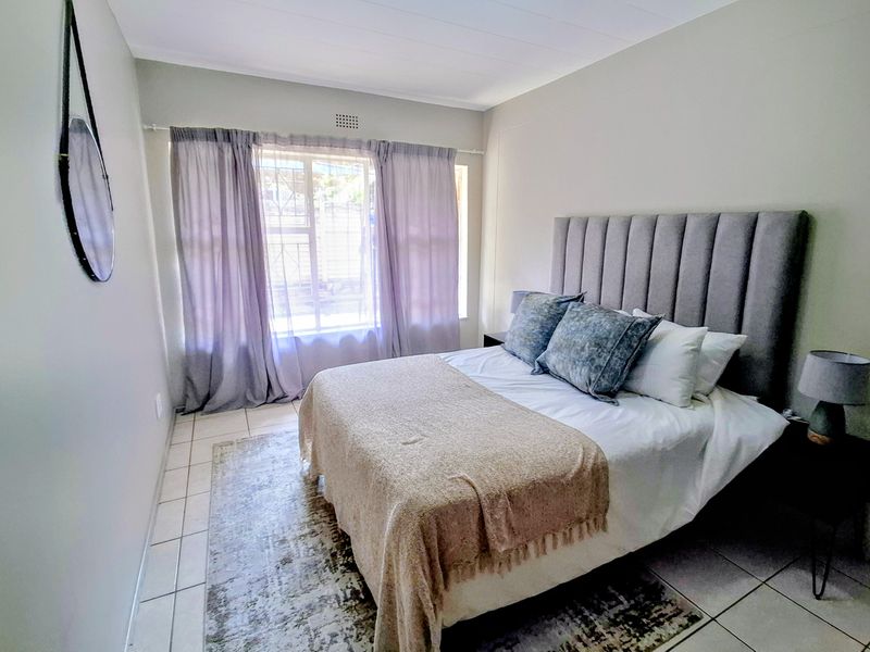 A well-maintained bedroom featuring neutral wall tones, tiled flooring, and a window fitted with security bars for added peace of mind.