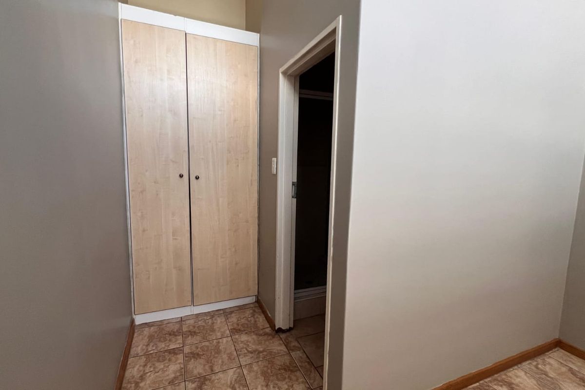 A clean, empty bedroom featuring built-in wooden cupboards, tiled flooring, and a doorway leading to an adjacent space.