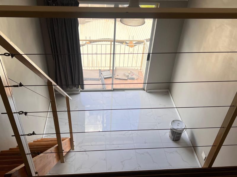 An open-plan living area featuring modern tiled flooring, a staircase with cable railing, and direct access to a balcony through sliding glass doors.