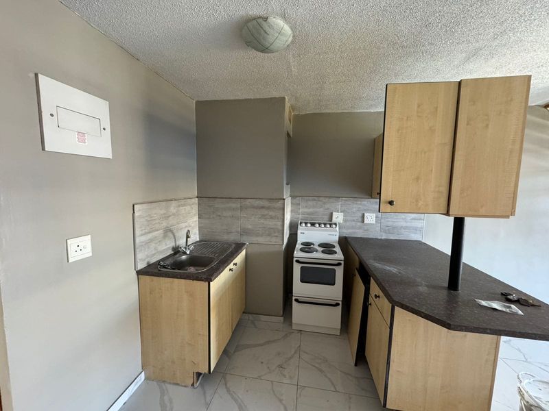 A compact kitchen featuring light wood-finish cabinetry, a stainless steel sink, a freestanding stove, and tiled flooring with a neutral backsplash.