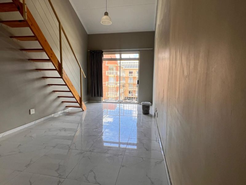 An empty living area featuring a wooden staircase, marble-look floor tiles, and a sliding glass door leading to a balcony.