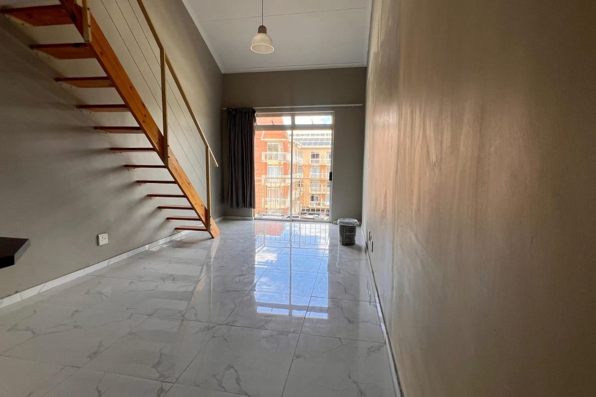 An empty living area featuring a wooden staircase, marble-look floor tiles, and a sliding glass door leading to a balcony.