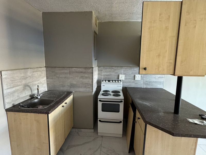 A compact kitchen featuring light wood-finish cabinetry, a freestanding stove, tiled backsplash, and marble-look floor tiles, currently in need of minor repairs and updates.