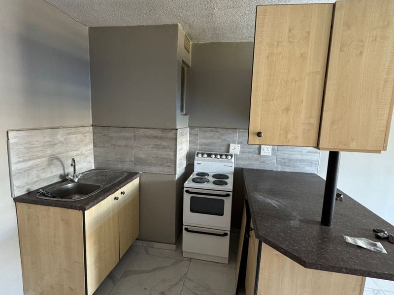 Compact kitchen featuring light wood-finish cabinetry, dark laminate countertops, tiled flooring, and a freestanding electric stove.