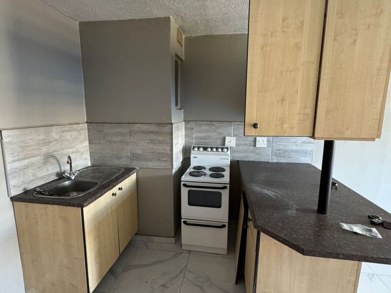 A compact kitchen featuring light wood-finish cabinetry, a freestanding stove, and modern marble-look floor tiles, currently awaiting final finishing touches.