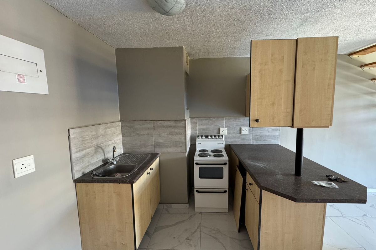 Compact kitchen featuring laminate cabinetry, tiled backsplash, stainless steel sink, and a freestanding stove, with tiled flooring throughout.